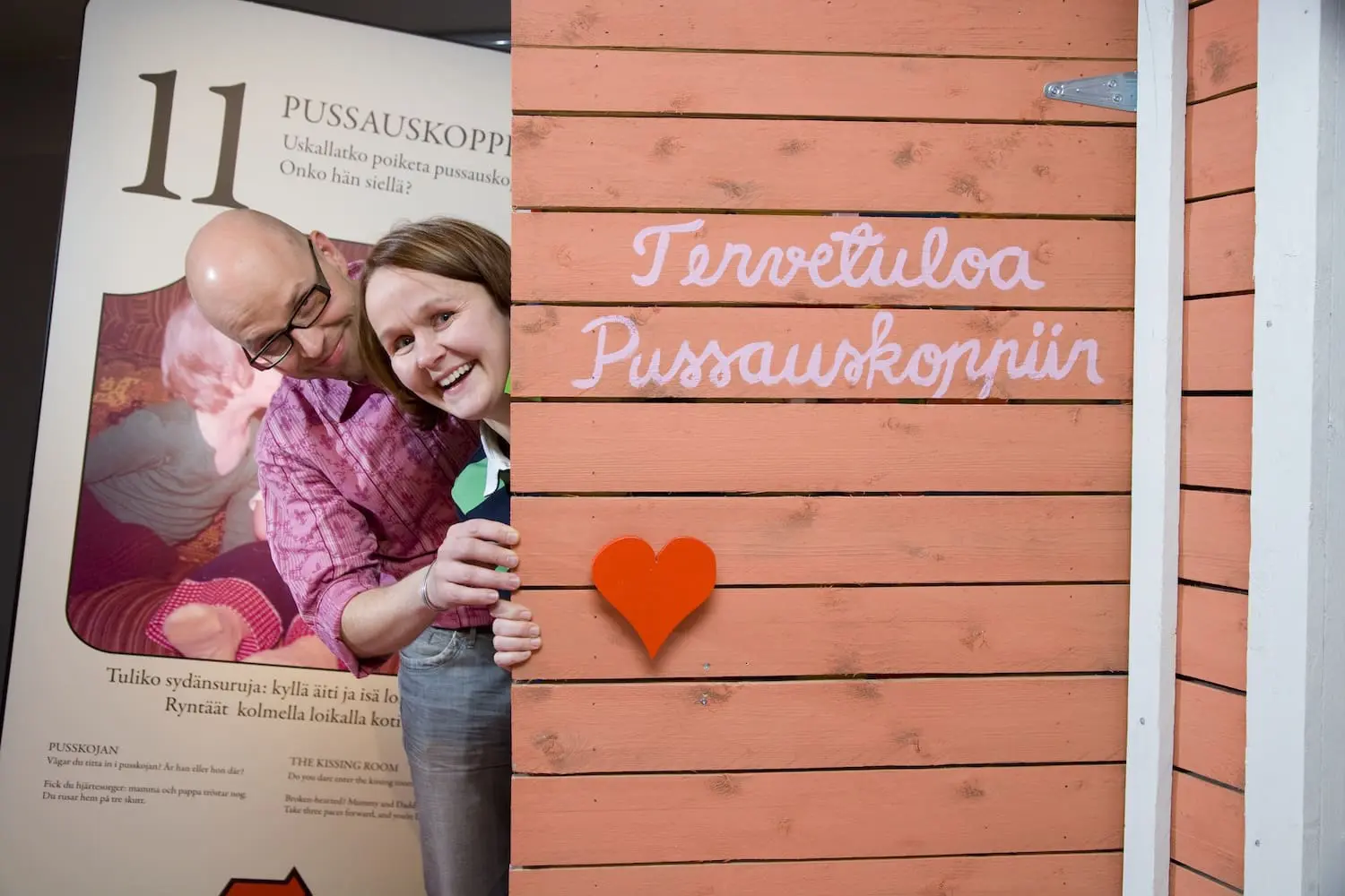 Mies ja nainen kurkistavat hymyillen pussauskopista.