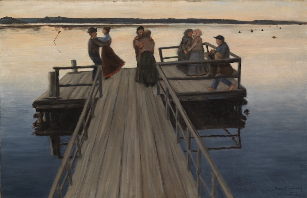 Kolme paria tanssii laiturilla veden äärellä, yksi henkilö katselee. 