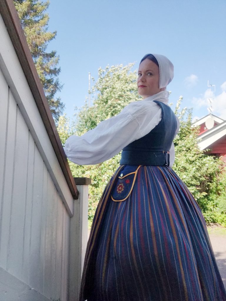 Valokuvassa naisella päällä sininen kansallispuku ja päässä valkoinen liinalakki.
