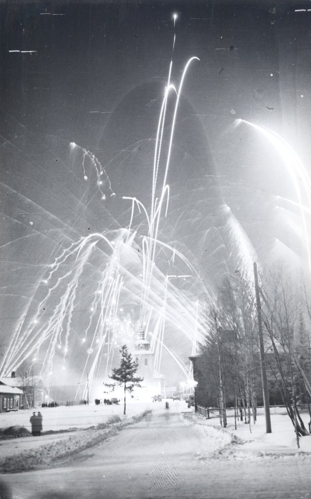 Black and white photograph shows a townscape in the light of tall fireworks on the occasion of Mänttä becoming a township. It was celebrated with fireworks in the temperature of minus 30 degrees centigrade on New Year’s Night 1 January 1948. The township became a city on 1 Jan 1973. Gösta Serlachius Fine Arts Foundation, Serlachius Museums, Photograph collections.