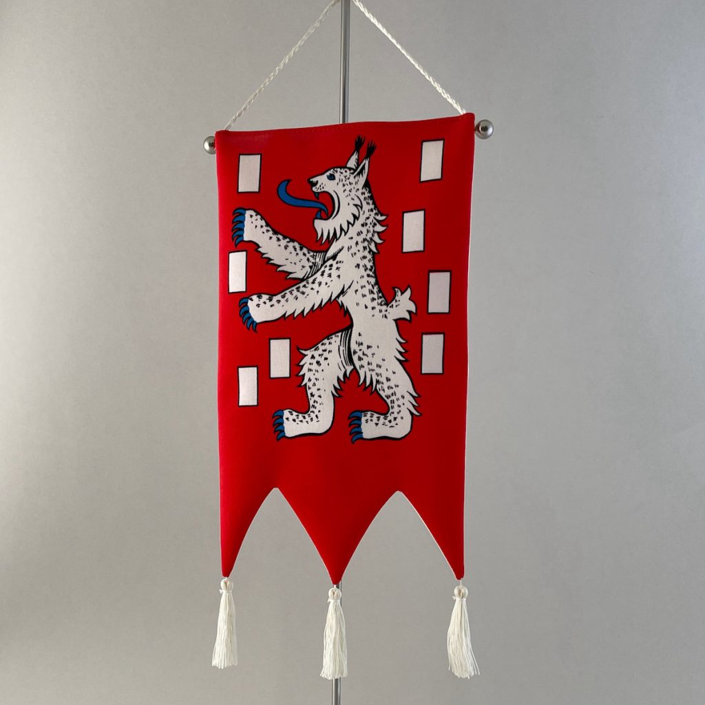 The table pennant of the City of Mänttä contains the coat of arms of the city in which a white lynx standing sideways on its two feet refers to the coat of arms of Häme Region and the silvery flags surrounding it to the paper mills. A plaque attached to the marble stand says: ”To Gustaf Serlachius 10 Dec 1986 Mänttä City”. The table pennant’s manufacturer is Taitopaino Oy.