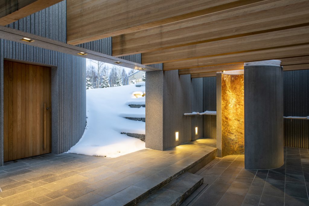 Grey stone material and warm oak finishings at Serlachius' Art Sauna's outdoor shower contrasted against a snow covered flower bed in winter.