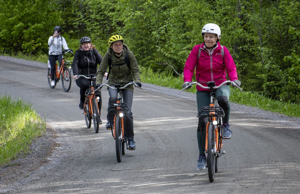 A group of people waring helmets and colorful clothing cycling on a gravel road amid summer nature.