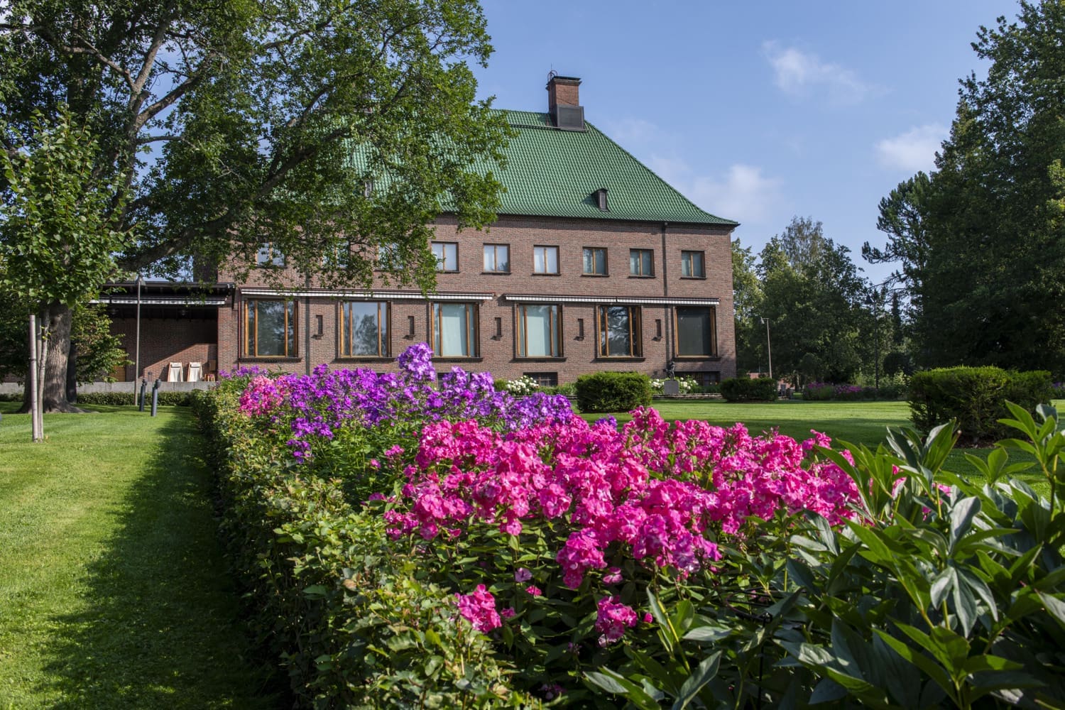 Serlachiusten kartano ulkopuolelta kuvattuna, kaunis kesäpäivä, pinkkejä kukkia etualalla