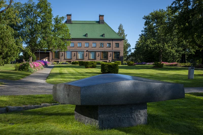 Kesäinen ulkokuva Veistospuistossa kohti kartanorakennusta, etualalla kiviveistos.