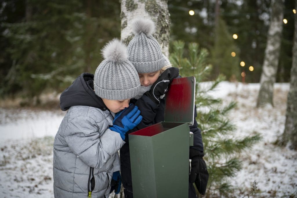 Lapset kurkistavat postilaatikkoon. talvisessa maisemassa.