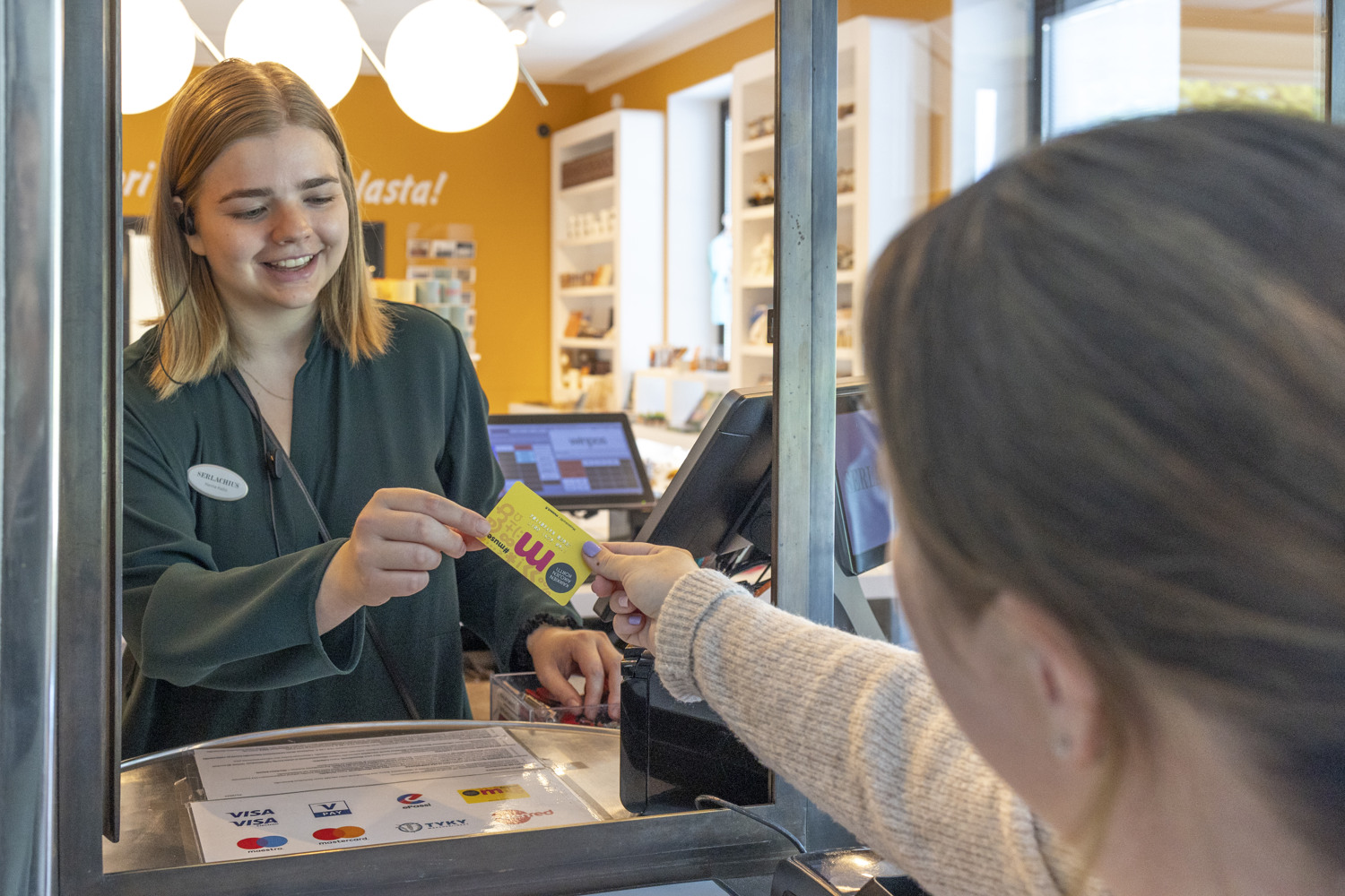 Nuori nainen myy pääsylippua toiselle naiselle museon lippukassalla.
