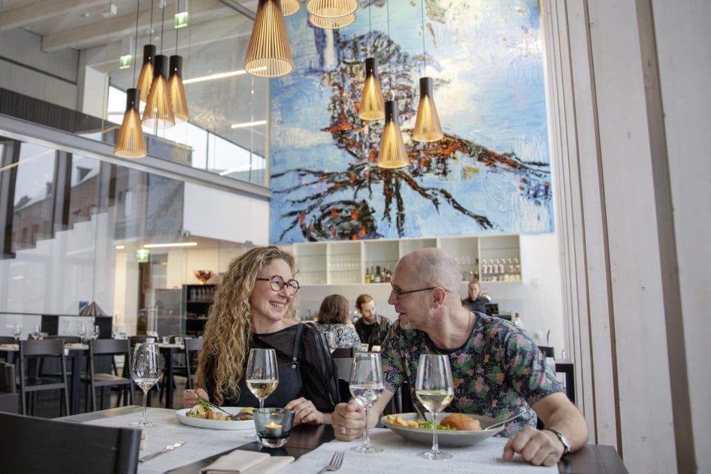 Nainen ja mies syömässä valoisassa ja korkeassa ravintolasalissa