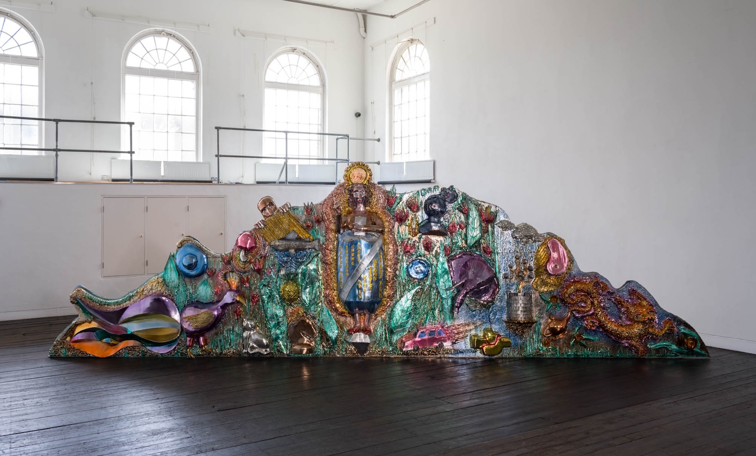 Korkeassa salissa koristeellinen ja monivärinen päätykolmiota esittävä teos.