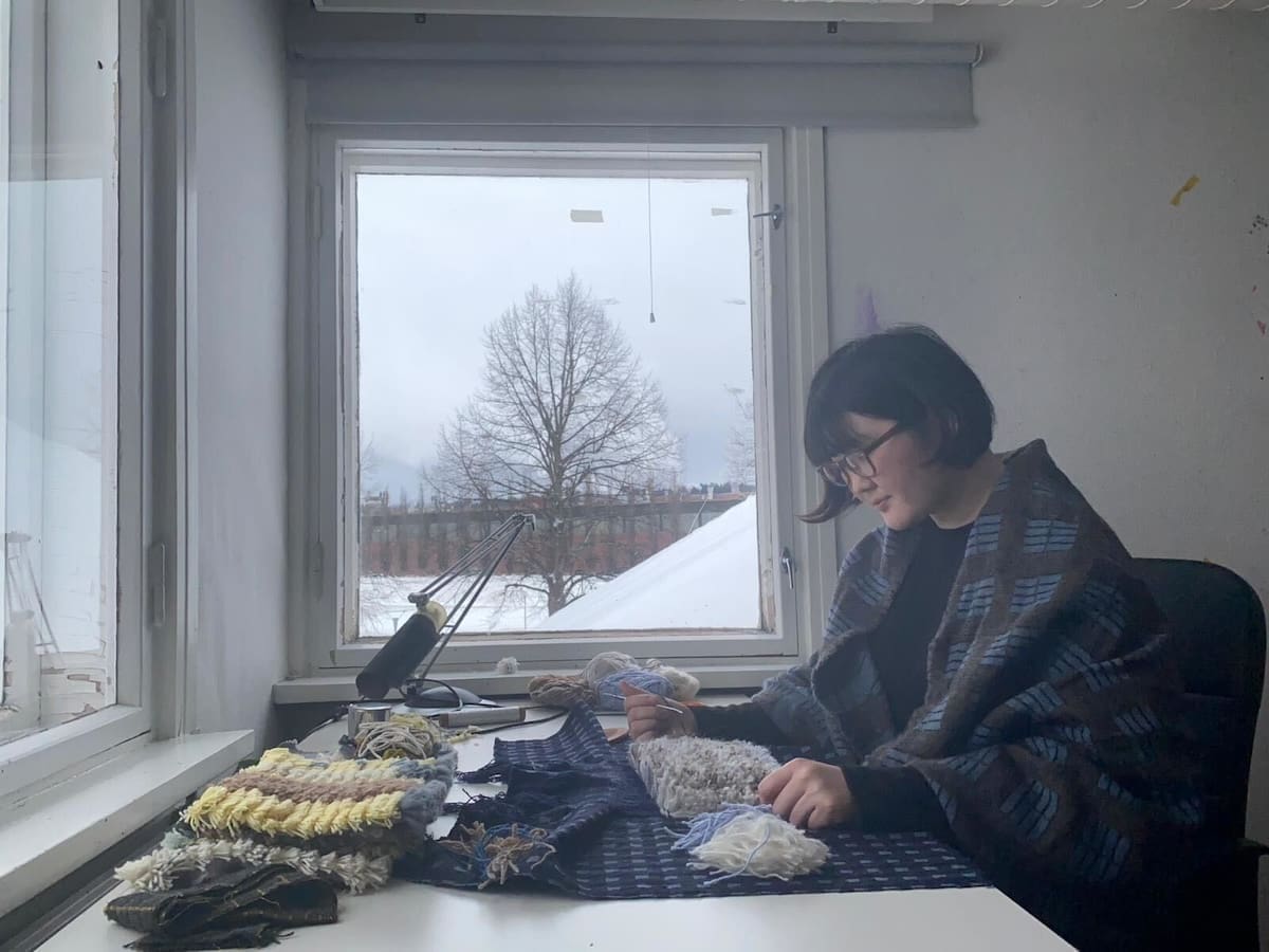 Nainen valmistaa ryijyä ikkunan ääressä. 