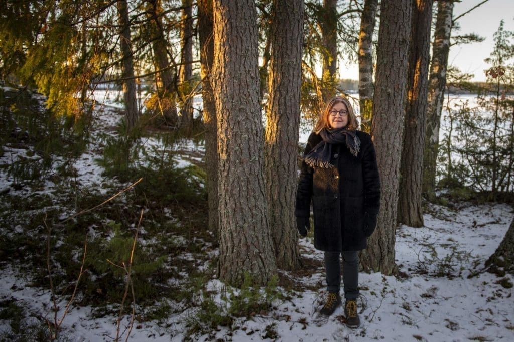 Eija-Liisa Ahtila seisoo talvisessa metsässä puiden edessä.