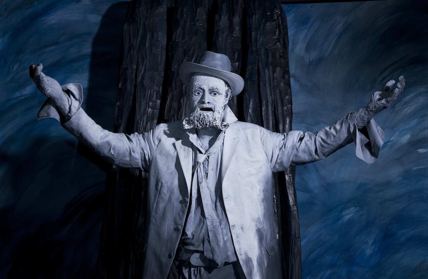 Paperista valmistettu patsas parrakkaasta vanhasta miehestä hattu päässä suu auki ja kädet ylhäällä