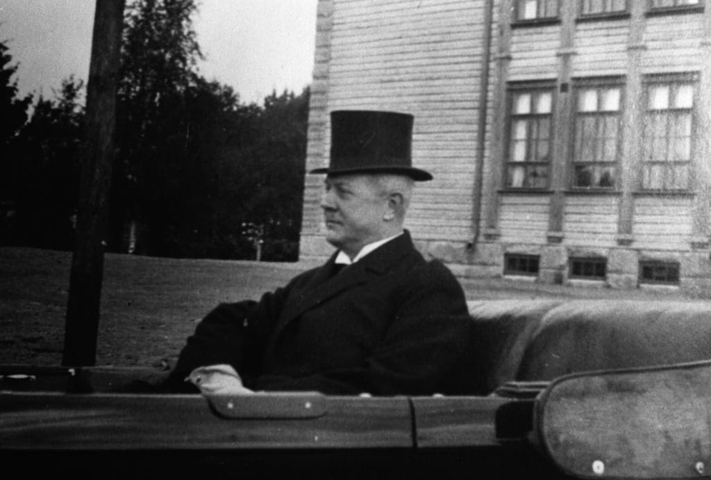 Gösta Serlachius istuu avoauton kyydissä silinterihattu päässä.