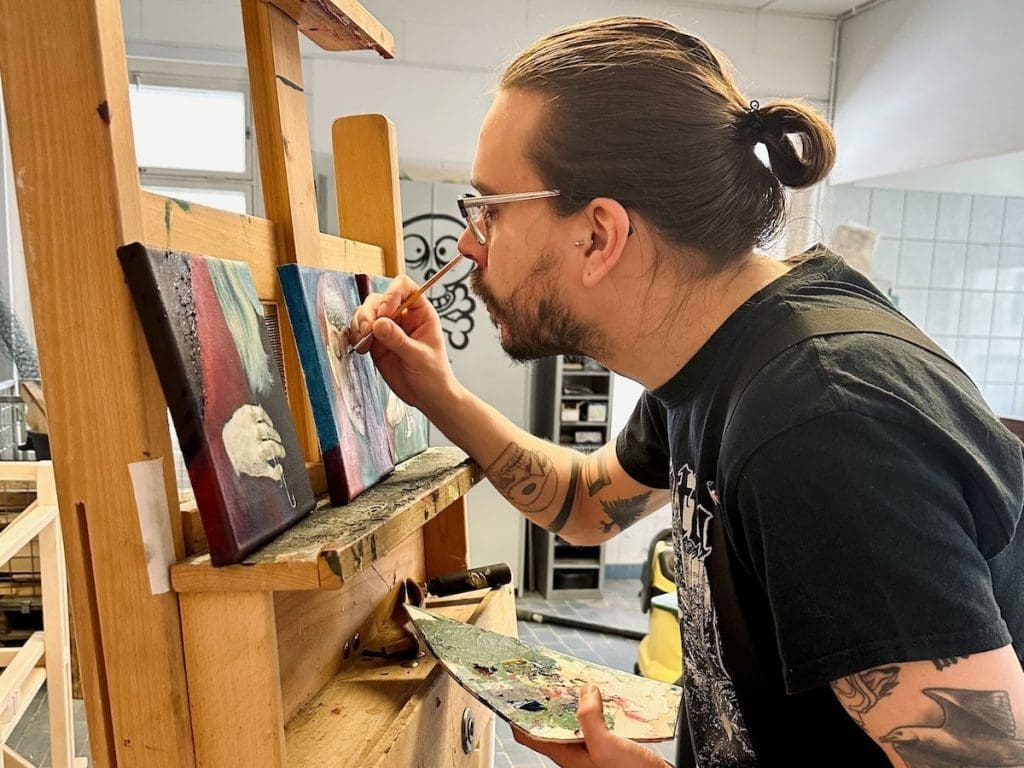 Artist painting an artwork on an easel in a studio.