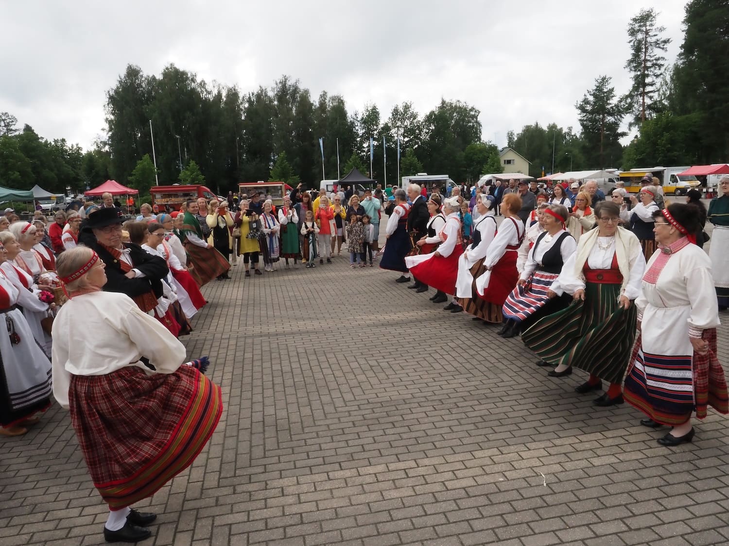 Kansallispukuiset ihmiset tanhuavat kahdessa rivissä ulkona.