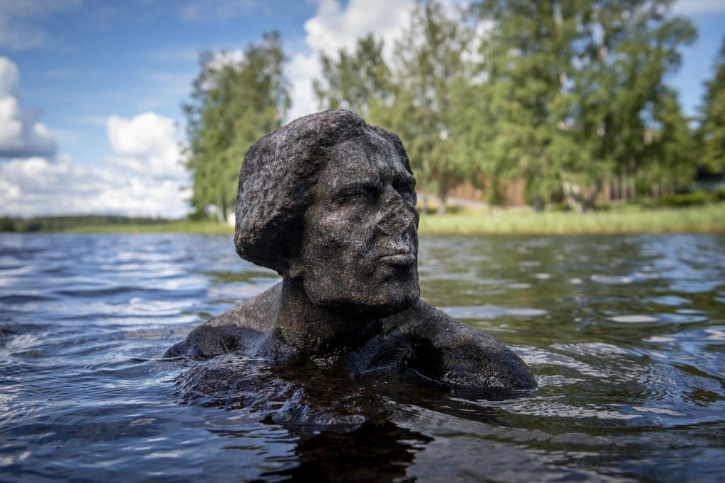 Miehen päätä ja hartioita kuvaava veistos veden keskellä.
