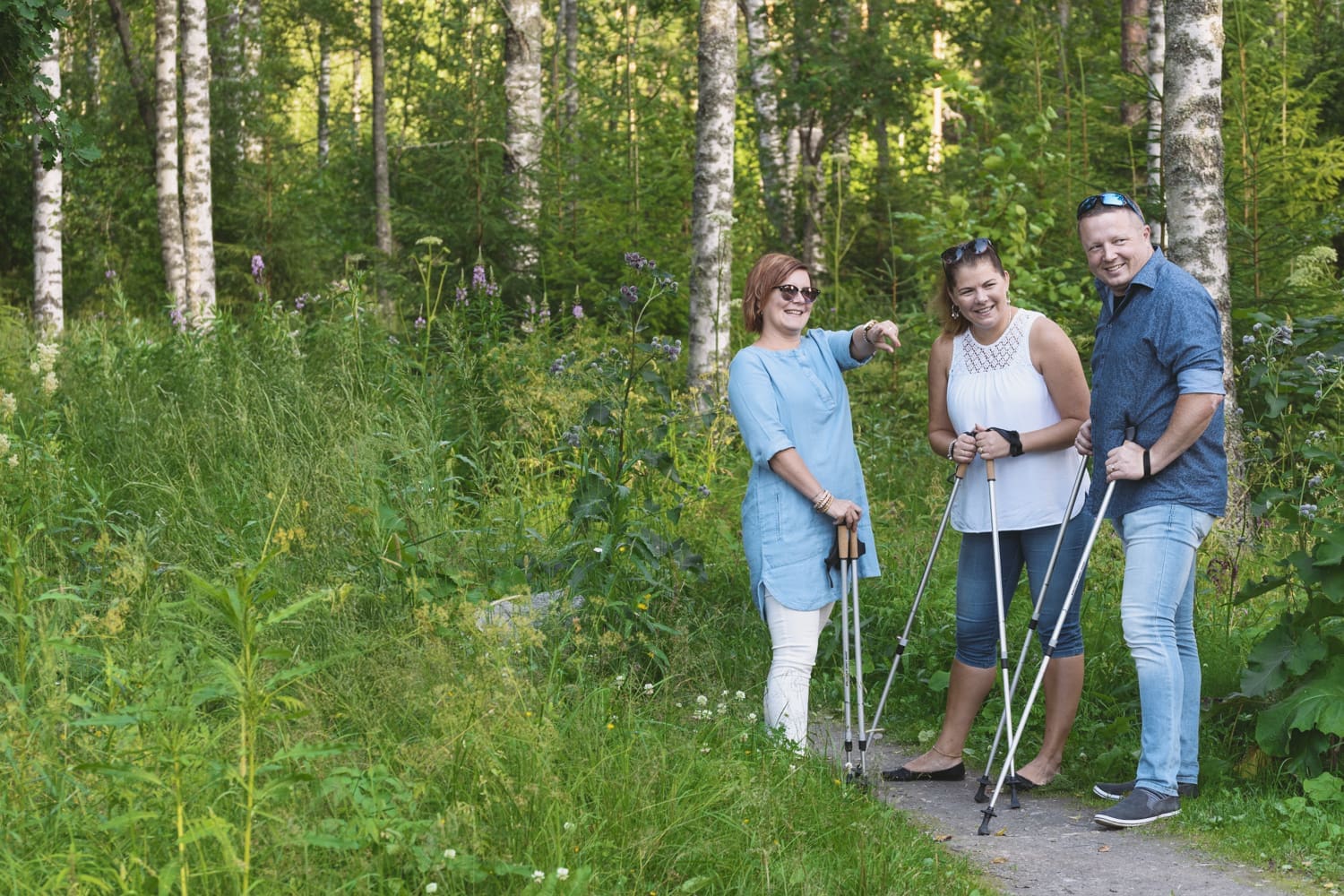 Kolme aikuista kävelysauvojen kanssa metsäpolulla, kesällä. 