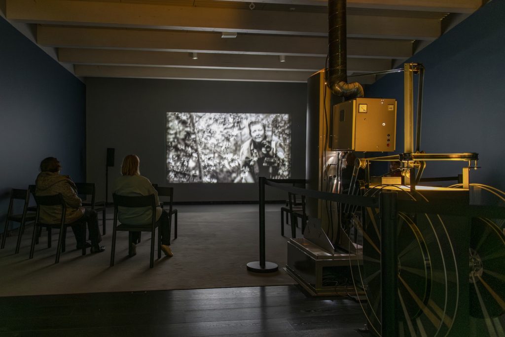 Ihmiset katsovat projektorilta näytetettävää elokuvaa pienessä tilassa.