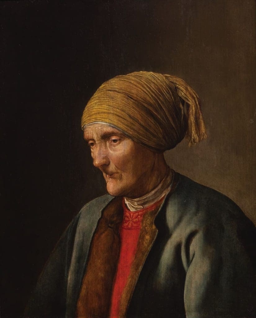 Portrait of an old woman dressed in a grain jacket and read blouse wearing a yellow scarf round her head.