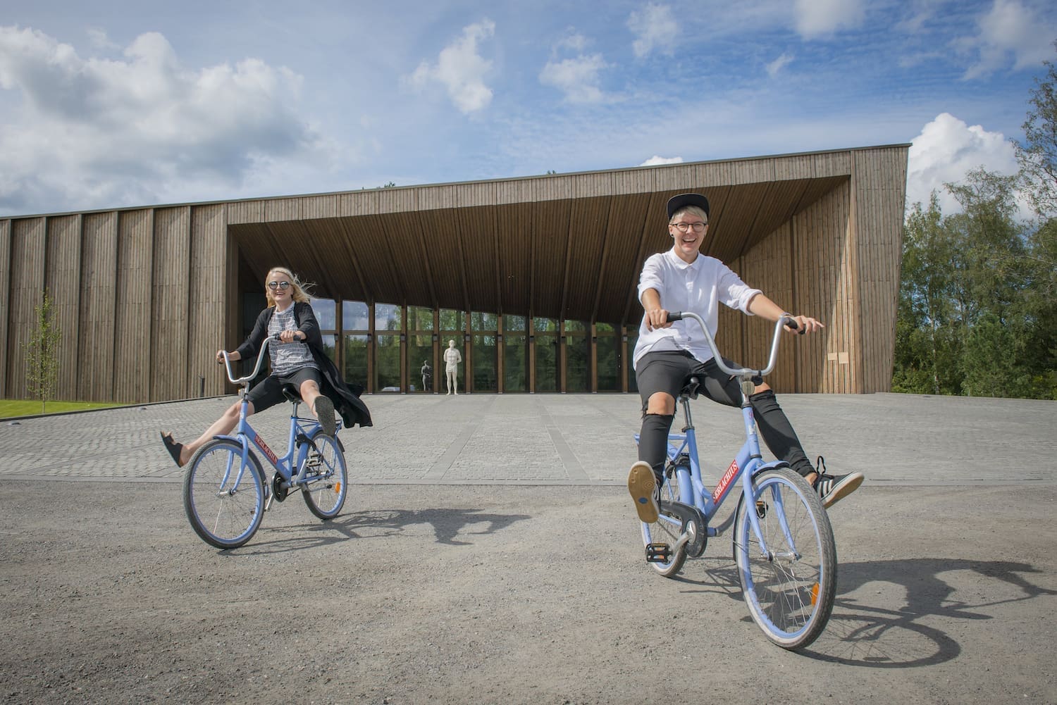Two persons riding bikes at the yard of Serlachius Manor with smiles on their faces