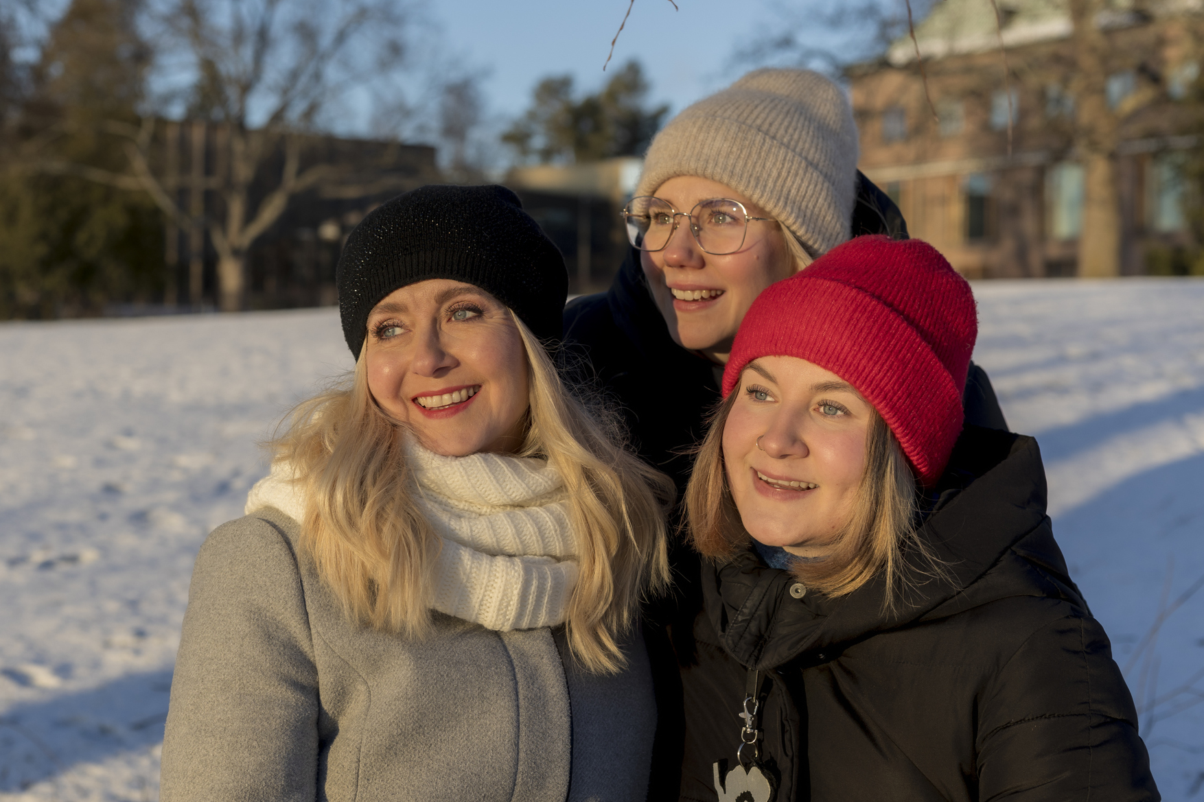 Kolme naista lähikuvassa, ulkovaatteet päällä talvisessa puistossa.
