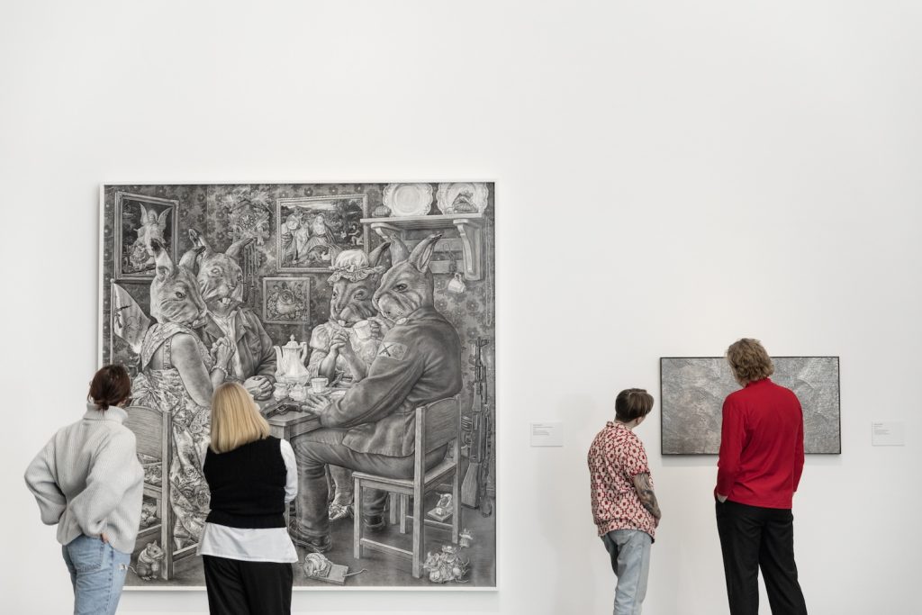 Neljä ihmistä katsoo selin kameraan kahta piirroskuvaa seinällä.