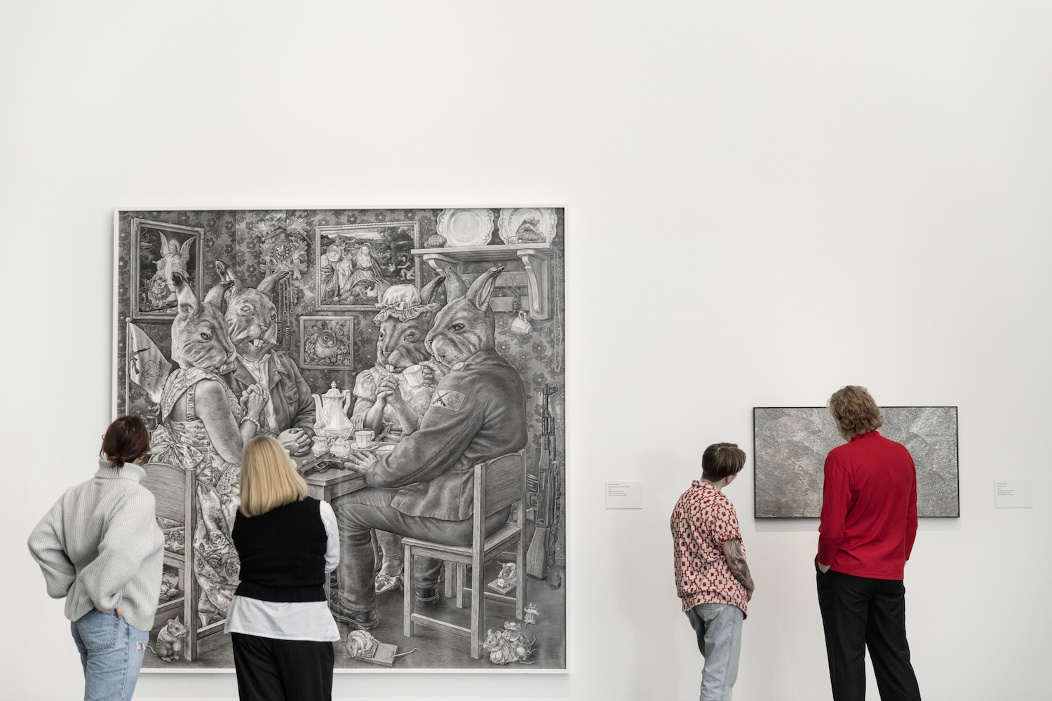 Neljä ihmistä katsoo selin kameraan kahta piirroskuvaa seinällä.