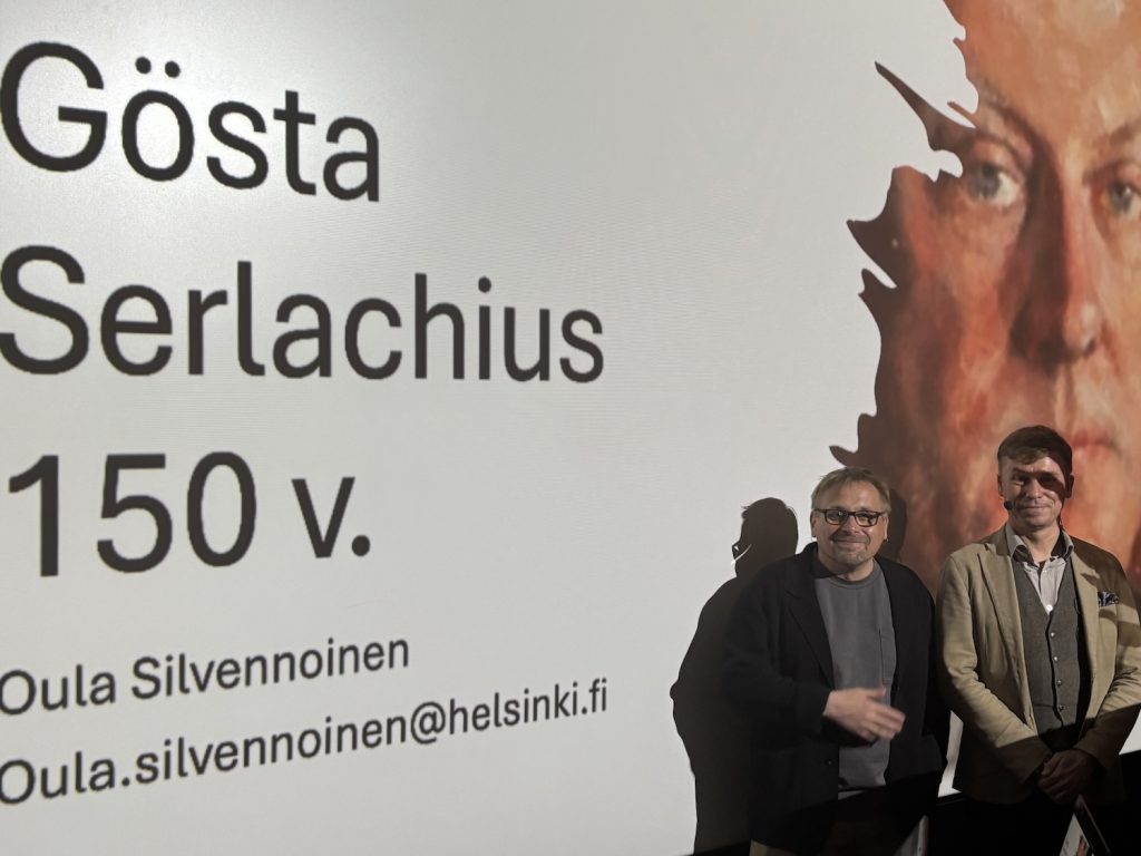 Kaksi miestä seisoo valkokankaan edessä.