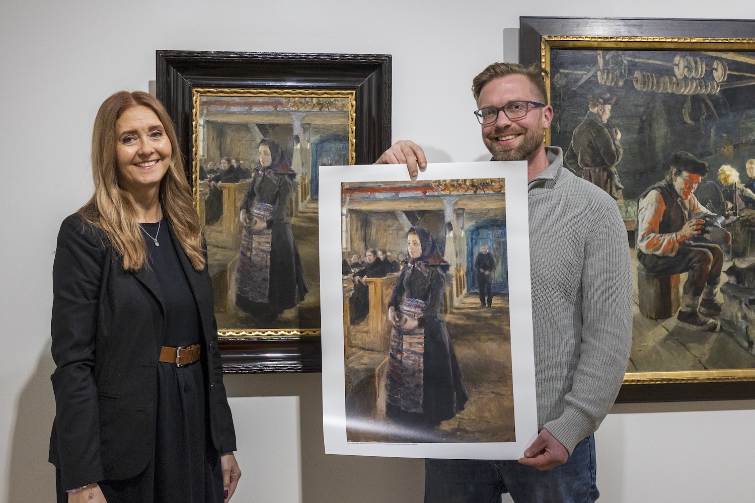 A woman and a man standing in front of an art work holding a poster made of the artwork in their hand.