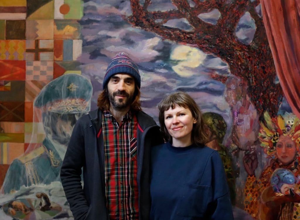 Artist couple standing in front of a landscape painting.