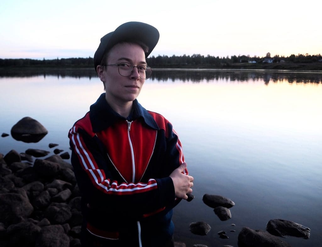 Henkilö katsoo tyynessä järvimaisemassa suoraan kameraan.