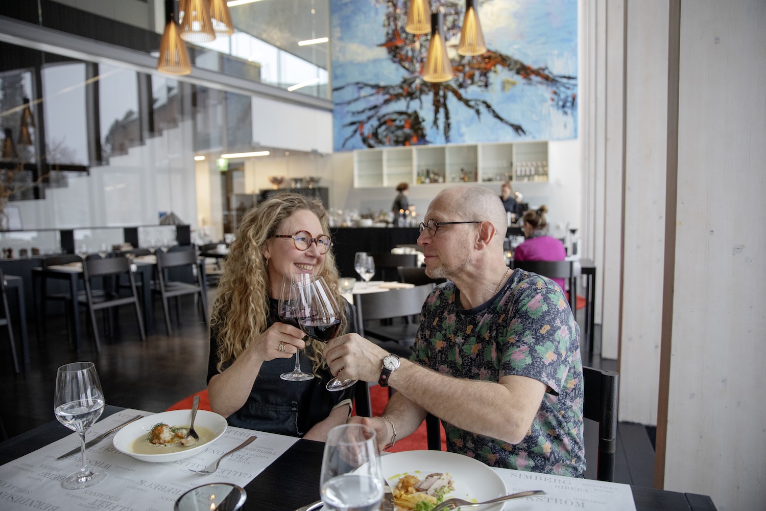 Mies ja nainen kippistävät viinilasejaan ravintolassa.