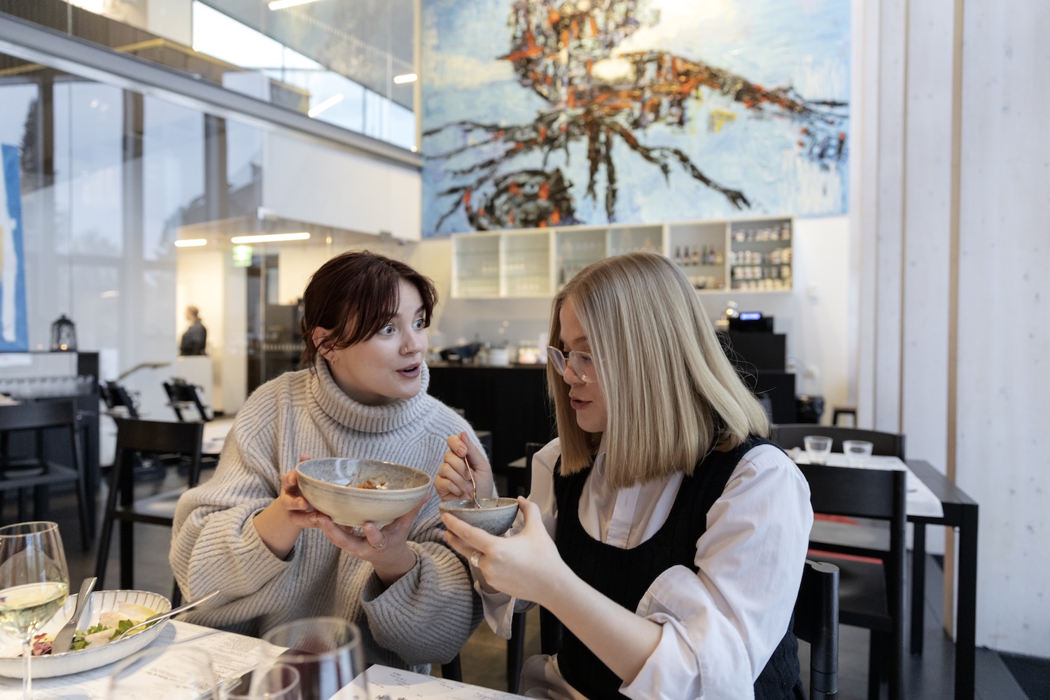 Kaksi nuorta naista syö ravintolan pöydässä ja katsovat toisiaan.