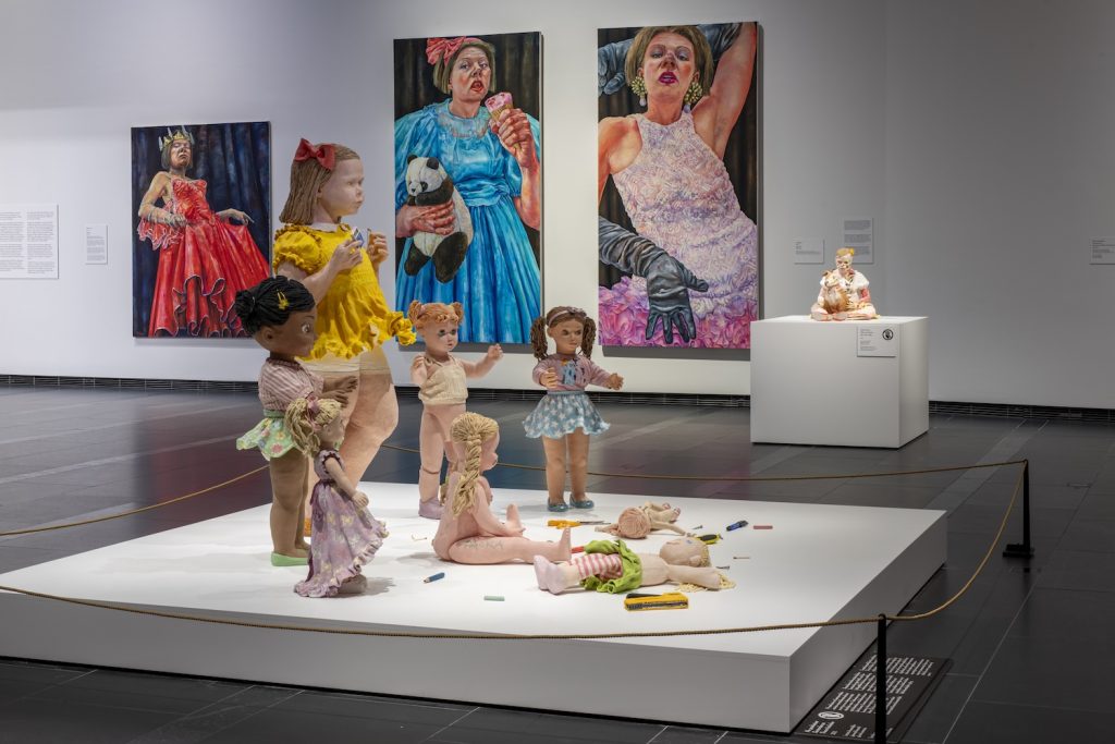 Kuvassa etualalla moniosainen veistossarja, jossa kuvataan pieni tyttö ja nukkeja.