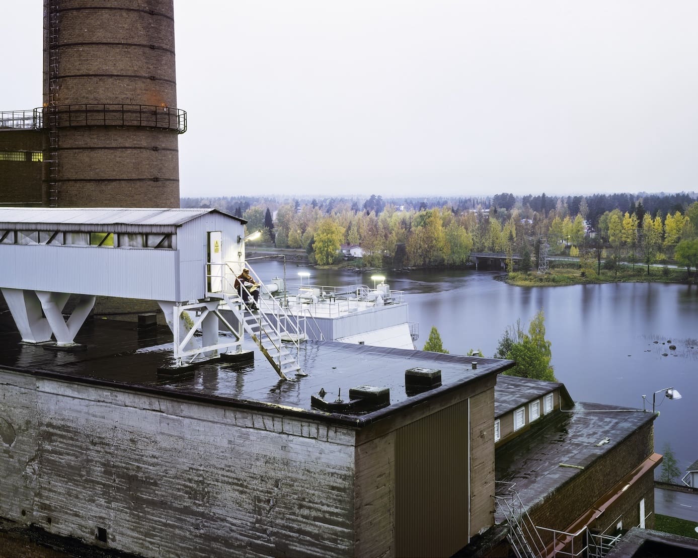Kuva miehestä lukemassa sanomalehteä tehtaan katolla olevan rakennuksen portailla